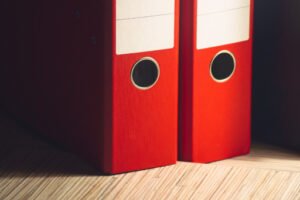 Two red binder folders neatly arranged on a wooden surface, symbolizing the meticulous documentation involved in the Affidavit of Support process.