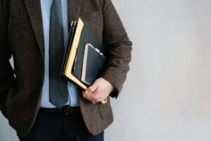 A mid-section view of an immigration lawyer in a woolen coat, light blue shirt, grey tie, and navy pants, holding a notebook and paperwork, showcasing expertise in managing the Affidavit of Support process.