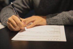 A close-up of a hand holding a pen and diligently filling out the Affidavit of Support form on a sleek black tabletop.