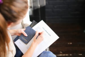 girl filling visa application form, student sitting on grey chair with passport