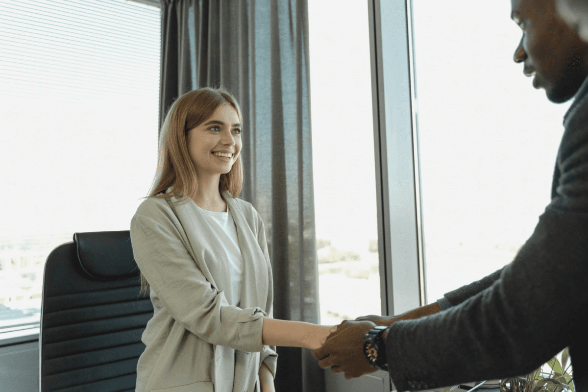  An international graduate in professional attire shaking hands with a hiring manager in a modern office.