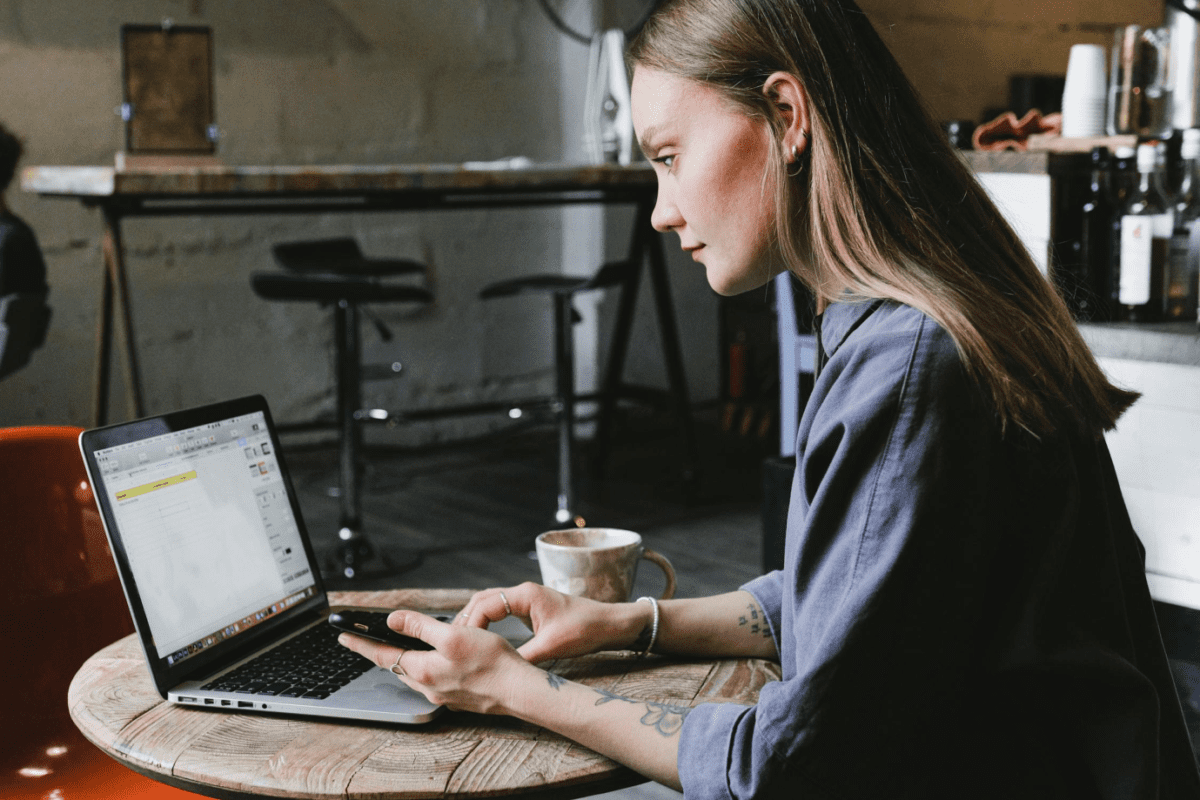 A recent international graduate sitting at a café, researching H-1B visa options on a laptop.