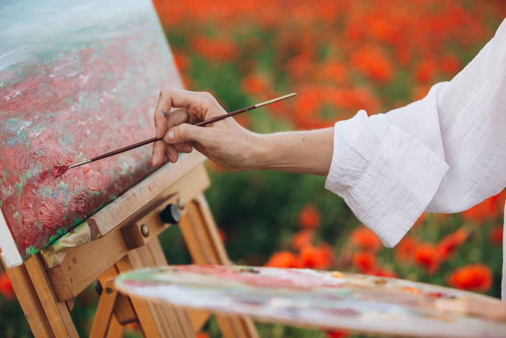 Female artist painting in a beautiful poppy field, adding vibrant colors to her canvas inspired by nature